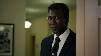 Movie still from “True Detective” (2014), created by Issa López – A man wearing a suit and tie standing in a room; Close Up shot, Over the shoulder angle