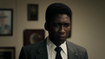 Movie still from “True Detective” (2014), created by Issa López – A man wearing a suit and tie in front of a wall; Close Up shot, Over the shoulder angle