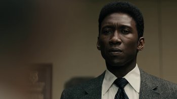 Movie still from “True Detective” (2014), created by Issa López – A man wearing a suit and tie in front of a wall; Close Up shot, Low angle