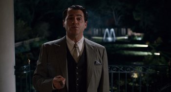 Movie still from “Trumbo” (2015), directed by Jay Roach – A man in a suit and tie standing in front of a fountain; Medium shot, Over the shoulder angle