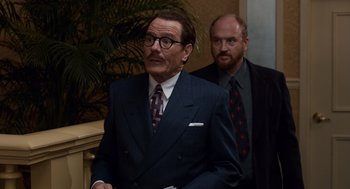 Movie still from “Trumbo” (2015), directed by Jay Roach – A man in a suit and tie standing next to another man in a suit and tie; Medium shot, Over the shoulder angle