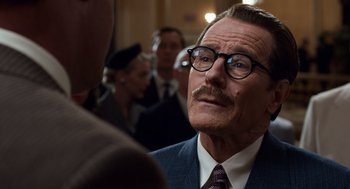 Movie still from “Trumbo” (2015), directed by Jay Roach – An older man in a suit and glasses; Close Up shot, Over the shoulder angle