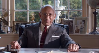 Movie still from “Trumbo” (2015), directed by Jay Roach – An older man sitting at a desk in a suit and tie; Medium shot, Low angle