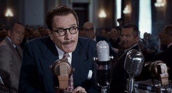 Movie still from “Trumbo” (2015), directed by Jay Roach – A man in a suit and tie sitting in front of a microphone; Close Up shot, Over the shoulder angle