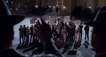Movie still from “Trumbo” (2015), directed by Jay Roach – A crowd of people holding signs in front of a building; Extreme Wide shot, High angle