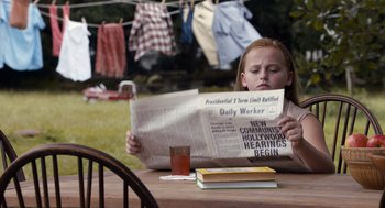 Movie still from “Trumbo” (2015), directed by Jay Roach – A young girl sitting at a table reading a newspaper; Medium shot, Over the shoulder angle