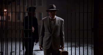 Movie still from “Trumbo” (2015), directed by Jay Roach – An older man in a suit and hat holding a suitcase; Wide shot, Low angle