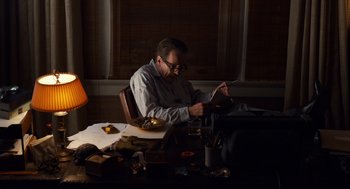 Movie still from “Trumbo” (2015), directed by Jay Roach – A man sitting at a table looking at a book; Medium shot, Low angle