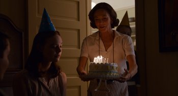 Movie still from “Trumbo” (2015), directed by Jay Roach – A woman holding a birthday cake with lit candles; Medium shot, Over the shoulder angle