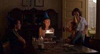 Movie still from “Trumbo” (2015), directed by Jay Roach – A girl in a party hat blows out a candle on a birthday cake; Medium shot, Over the shoulder angle