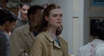Movie still from “Trumbo” (2015), directed by Jay Roach – A young woman in a trench coat standing in front of a group of people; Close Up shot, Over the shoulder angle