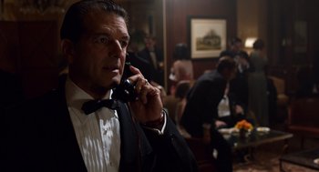 Movie still from “Trumbo” (2015), directed by Jay Roach – A man in a tuxedo talking on a phone; Medium shot, Over the shoulder angle