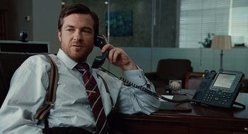 Movie still from “Up in the Air” (2009), directed by Jason Reitman – A man sitting at a desk talking on a phone; Medium shot, Over the shoulder angle
