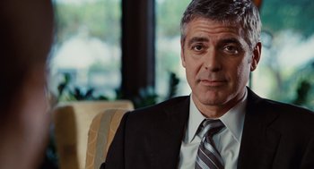 Movie still from “Up in the Air” (2009), directed by Jason Reitman – A man wearing a suit and tie sitting in a chair; Close Up shot, Over the shoulder angle