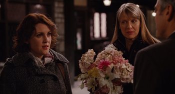 Movie still from “Up in the Air” (2009), directed by Jason Reitman – Two women standing next to each other holding flowers; Medium shot, Over the shoulder angle