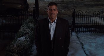 Movie still from “Up in the Air” (2009), directed by Jason Reitman – A man in a suit standing in front of a gate; Medium shot, Over the shoulder angle