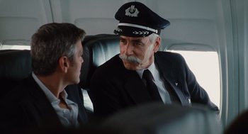 Movie still from “Up in the Air” (2009), directed by Jason Reitman – An older man in a suit and a hat sits next to a young man; Medium shot, Over the shoulder angle