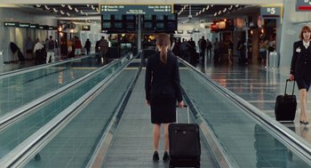 Movie still from “Up in the Air” (2009), directed by Jason Reitman – A woman in a black suit is pulling a black suitcase; Wide shot, High angle