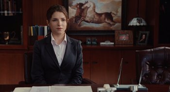Movie still from “Up in the Air” (2009), directed by Jason Reitman – A woman sitting at a desk in front of a painting; Medium shot, Over the shoulder angle