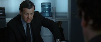 Movie still from “V for Vendetta” (2005), directed by James McTeigue – A man wearing a suit and tie leaning on a table; Close Up shot, Over the shoulder angle