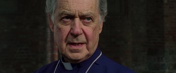 Movie still from “V for Vendetta” (2005), directed by James McTeigue – An older man wearing a priest's collar; Close Up shot, Low angle