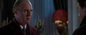 Movie still from “V for Vendetta” (2005), directed by James McTeigue – An older man wearing a suit and tie in front of a lamp; Close Up shot, Low angle