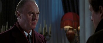 Movie still from “V for Vendetta” (2005), directed by James McTeigue – An older man wearing a suit and tie in front of candles; Close Up shot, Low angle