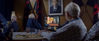 Movie still from “V for Vendetta” (2005), directed by James McTeigue – Two older men sitting in front of a television; Medium shot, Over the shoulder angle