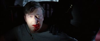 Movie still from “V for Vendetta” (2005), directed by James McTeigue – A man with blood on his face is sitting in a dark room; Close Up shot, Overhead angle