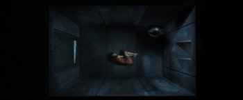 Movie still from “V for Vendetta” (2005), directed by James McTeigue – A person laying on the ground in a dark room; Extreme Wide shot, Overhead angle