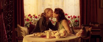 Movie still from “V for Vendetta” (2005), directed by James McTeigue – Two women sitting at a table kissing each other; Medium shot, Low angle