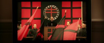 Movie still from “V for Vendetta” (2005), directed by James McTeigue – A man is giving a speech in front of a group of people; Medium shot, Over the shoulder angle