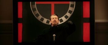Movie still from “V for Vendetta” (2005), directed by James McTeigue – A man in a black jacket is holding a microphone; Medium shot, Over the shoulder angle