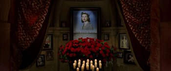 Movie still from “V for Vendetta” (2005), directed by James McTeigue – A bunch of candles in front of a poster of a woman; Wide shot, High angle