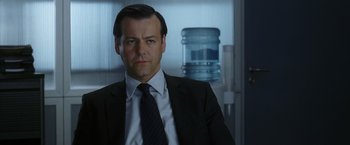 Movie still from “V for Vendetta” (2005), directed by James McTeigue – A man wearing a suit and tie in front of a water cooler; Close Up shot, Low angle