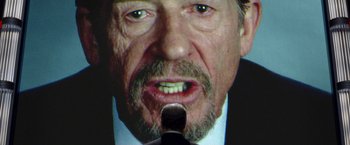 Movie still from “V for Vendetta” (2005), directed by James McTeigue – A man with a beard and a microphone in front of him; Extreme Close Up shot, Over the shoulder angle