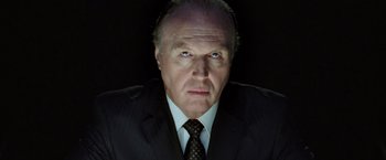 Movie still from “V for Vendetta” (2005), directed by James McTeigue – An older man in a suit and tie looking at the camera; Close Up shot, Low angle