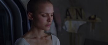 Movie still from “V for Vendetta” (2005), directed by James McTeigue – A woman with a shaved head is looking down; Close Up shot, Over the shoulder angle