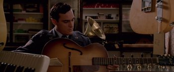 Movie still from “Walk the Line” (2005), directed by James Mangold – A man in uniform playing an instrument in a room; Medium shot, Over the shoulder angle