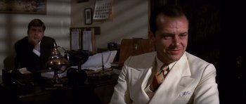 Movie still from “Chinatown” (1974), directed by Roman Polanski – A man in a suit sitting at a desk in front of papers; Medium shot, Over the shoulder angle