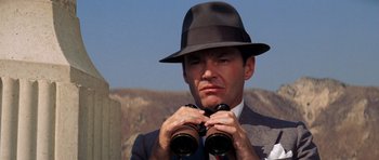 Movie still from “Chinatown” (1974), directed by Roman Polanski – A man in a suit and hat looking through binoculars; Close Up shot, Low angle