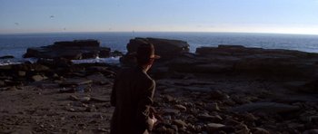 Movie still from “Chinatown” (1974), directed by Roman Polanski – A man in a hat is standing on the rocks by the water; Extreme Wide shot, High angle