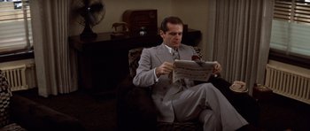 Movie still from “Chinatown” (1974), directed by Roman Polanski – A man sitting in a chair reading a newspaper; Medium shot, Low angle