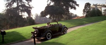 Movie still from “Chinatown” (1974), directed by Roman Polanski – An old car driving down a road near a tree; Wide shot, Low angle