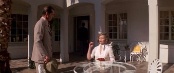 Movie still from “Chinatown” (1974), directed by Roman Polanski – A woman sitting at a table with a cigarette in her mouth; Medium shot, Over the shoulder angle