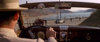 Movie still from “Chinatown” (1974), directed by Roman Polanski – An old car driving down a road with people standing on the side of the road; Wide shot, High angle