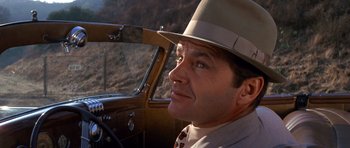Movie still from “Chinatown” (1974), directed by Roman Polanski – A person wearing a hat driving a car; Close Up shot, Over the shoulder angle
