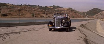 Movie still from “Chinatown” (1974), directed by Roman Polanski – An old car driving down a road near a body of water; Wide shot, High angle
