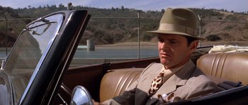 Movie still from “Chinatown” (1974), directed by Roman Polanski – A man sitting in the back seat of a car wearing a hat; Close Up shot, Over the shoulder angle