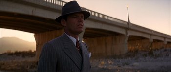 Movie still from “Chinatown” (1974), directed by Roman Polanski – A man in a suit and hat standing in front of a bridge; Close Up shot, Low angle